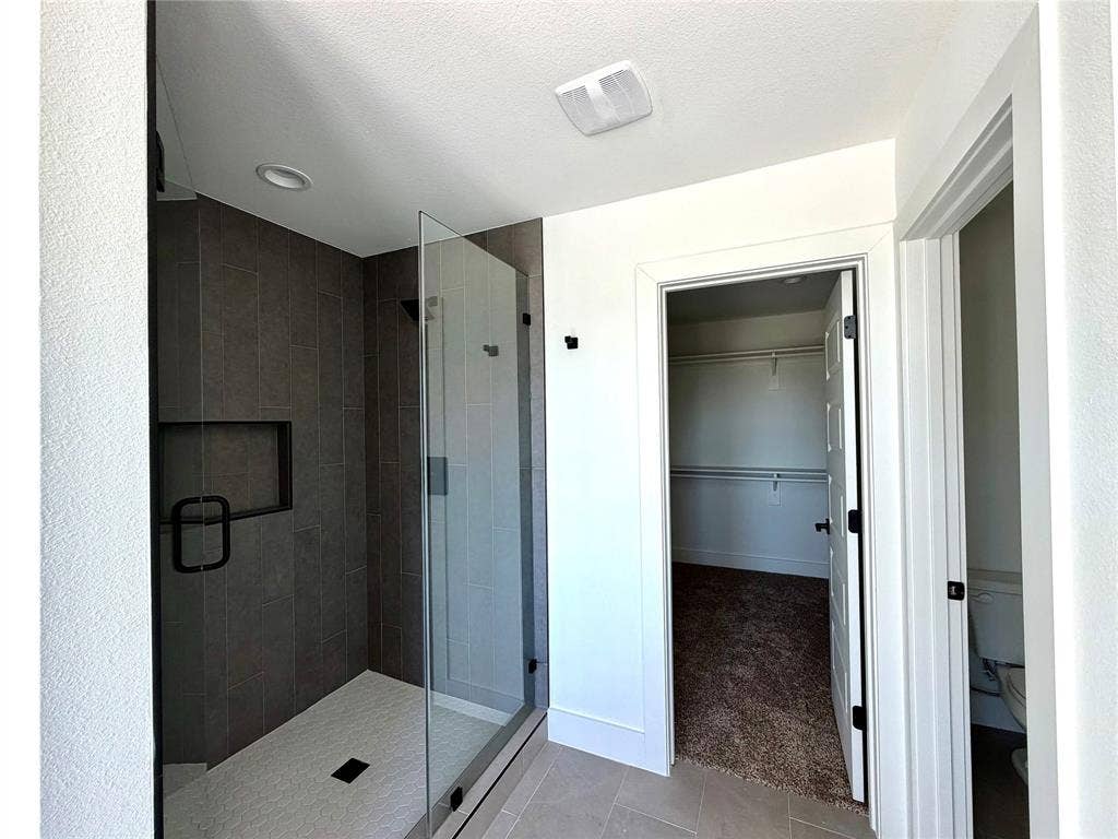8902 Lowell Street, Rowlett, TX 75089 Walk-in shower with dark ceramic tile surround, built-in shelving niche, glass enclosure, and matte black hardware, accompanied by a separate carpeted closet space
