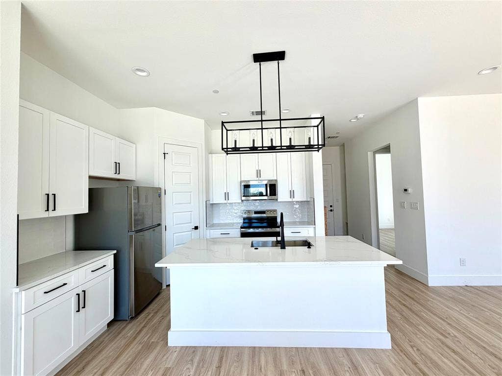 8902 Lowell Street, Rowlett, TX 75089 Kitchen featuring white cabinetry, center island with stone-finish countertop, stainless steel appliances, matte black hardware, and rectangular cage pendant lighting over wood-finish flooring