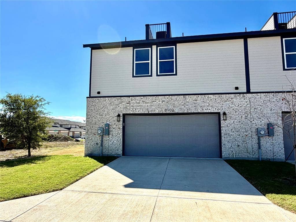 8902 Lowell Street, Rowlett, TX 75089 Exterior facade featuring stone veneer, horizontal siding, double-car garage, and a roof deck with metal railing