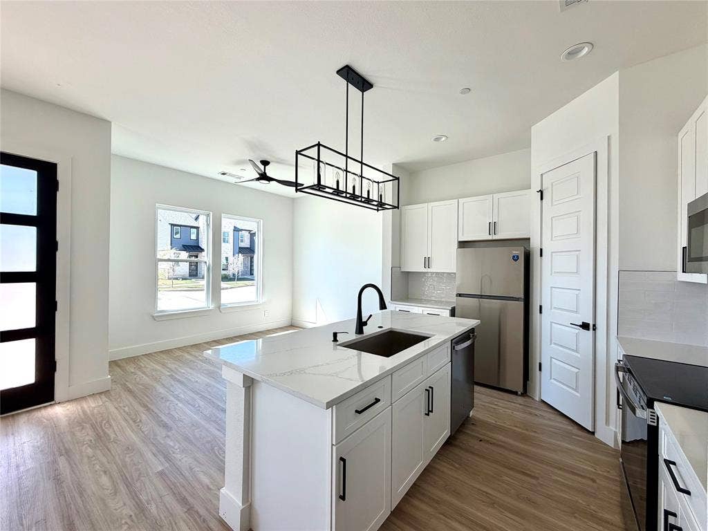 8902 Lowell Street, Rowlett, TX 75089 Kitchen featuring a central island with a stone countertop, white cabinetry, a matte black faucet, wood-finish flooring, and a linear pendant light fixture
