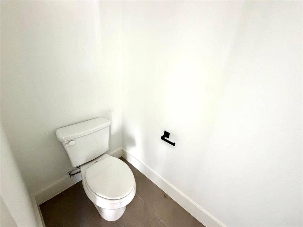 8902 Lowell Street, Rowlett, TX 75089 White vitreous china toilet, matte black toilet paper holder, and neutral large-format tile flooring