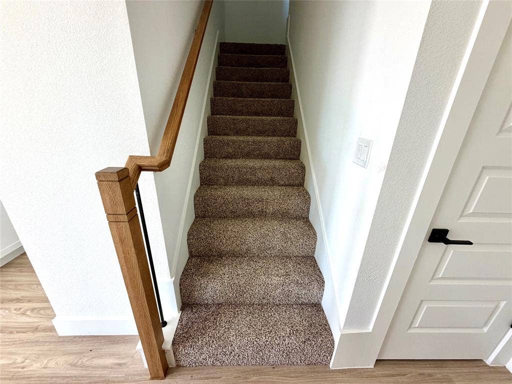 8902 Lowell Street, Rowlett, TX 75089 Staircase featuring wall-to-wall carpeting, wood-finish handrail, and matte black hardware on a four-panel interior door