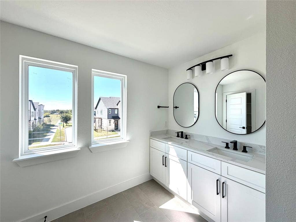 8902 Lowell Street, Rowlett, TX 75089 Dual-vanity cabinet with white shaker-style doors, light-toned stone countertop, dual undermount sinks, matte black hardware, and two circular mirrors