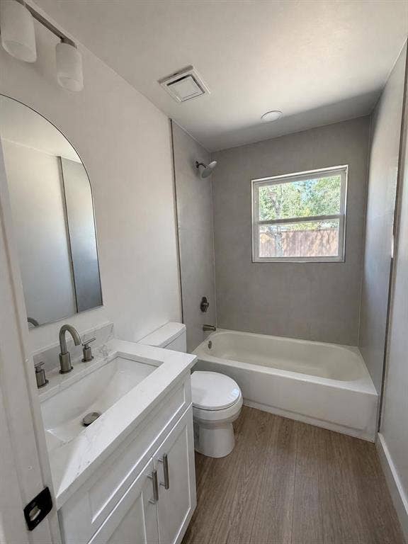Bathroom featuring a vanity with a white countertop and rectangular undermount sink, arched wall mirror, brushed nickel faucet hardware, and wood-finish flooring