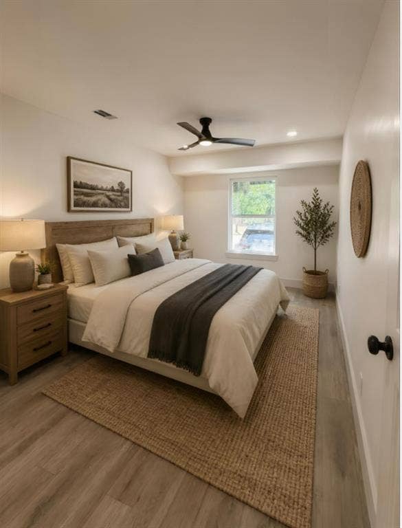Bedroom featuring wood-finish flooring, a matte black ceiling fan with integrated lighting, and a window with a neutral frame