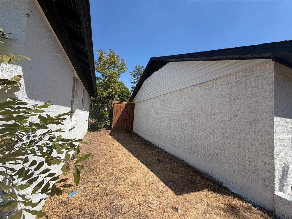 Exterior side yard featuring white painted brick masonry, horizontal siding gables, and a wood privacy gate