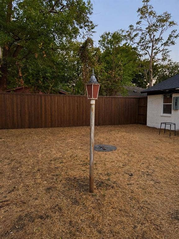 Backyard featuring a tall wood-finish privacy fence, a metal post-mounted lantern, and exterior white masonry