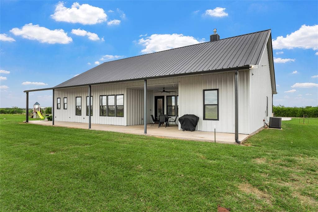 Metal-sided exterior featuring a standing seam metal roof, expansive covered concrete patio, and dark-framed windows