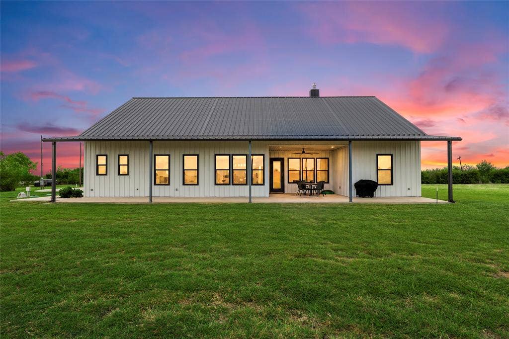 Modern exterior featuring vertical siding, a standing seam metal roof, a full-length covered patio, and large rectangular windows