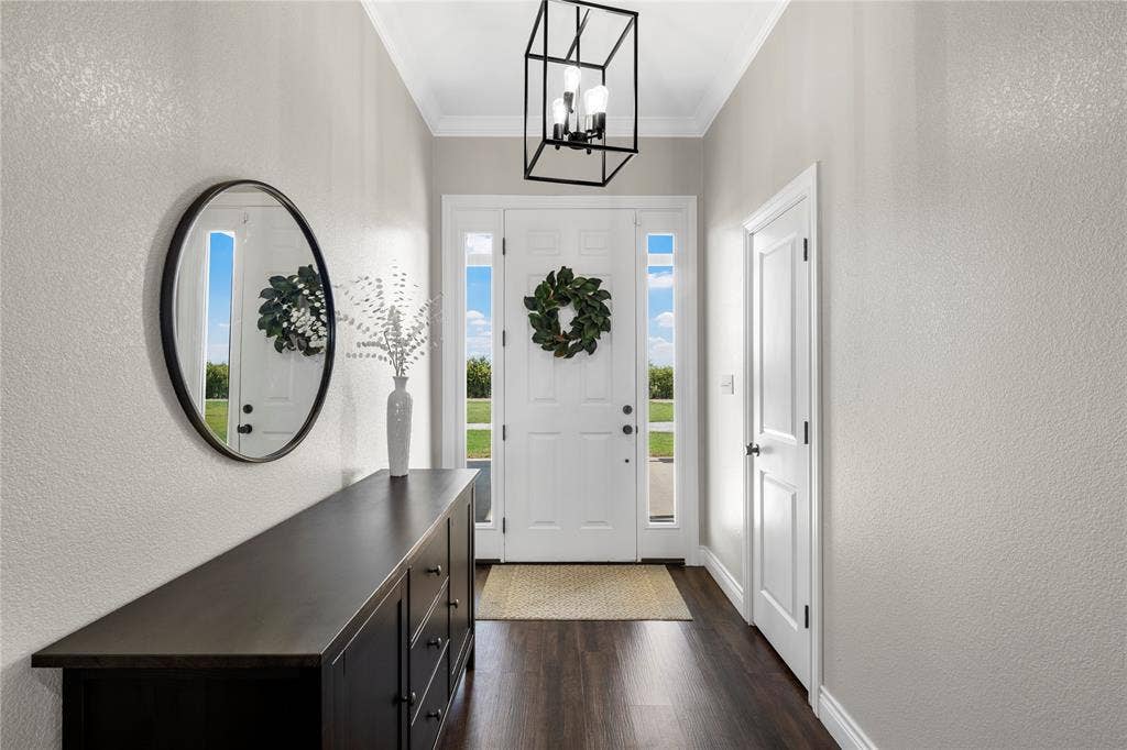 Foyer featuring wood-finish flooring, a white front door with flanking sidelights, crown molding, and a matte black geometric pendant light