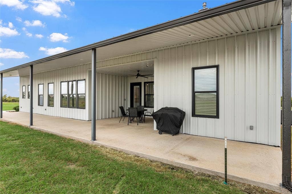 Covered concrete patio featuring metal vertical siding, black-framed windows, and a ceiling-mounted fan