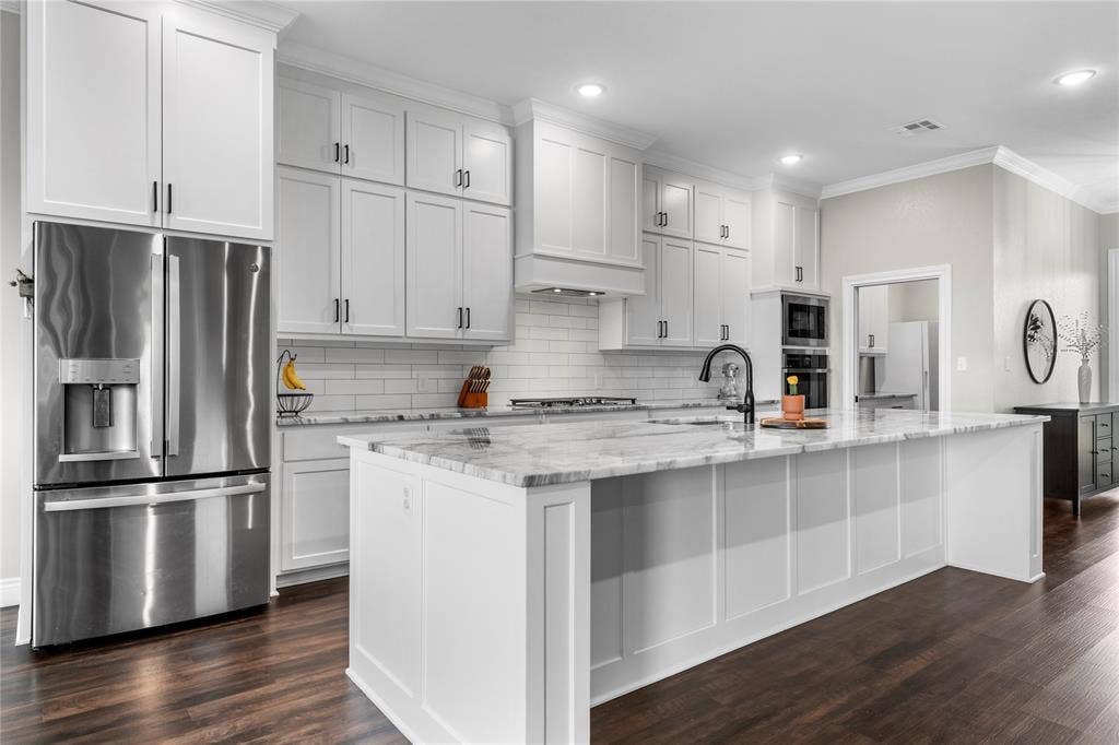 Kitchen featuring ceiling-height shaker cabinetry, stone-finish countertops, stainless steel appliances, a center island with sink, and wood-finish flooring