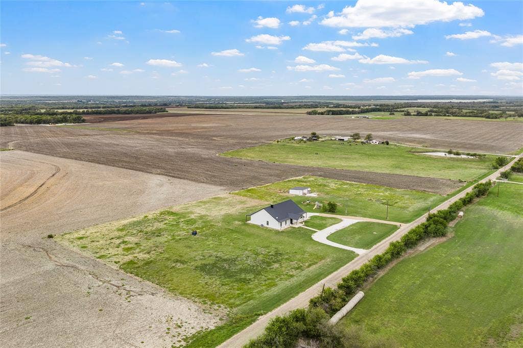 Aerial perspective of a rural property featuring a detached residence, a secondary outbuilding, a concrete driveway, and expansive acreage