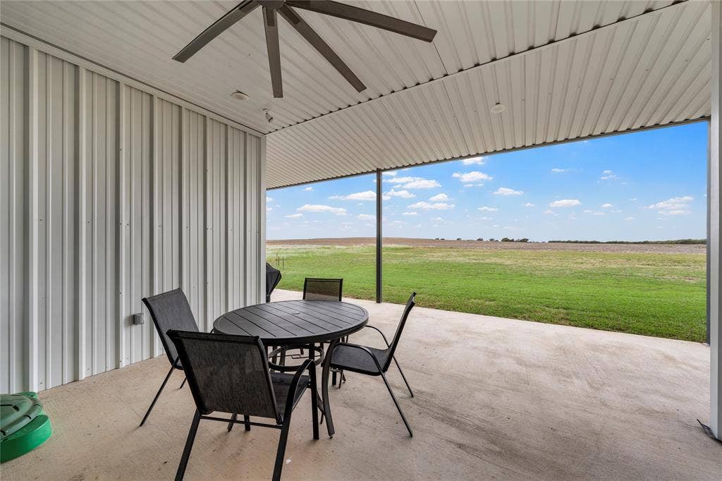 Covered concrete patio featuring vertical metal siding, a ceiling fan, and expansive open acreage