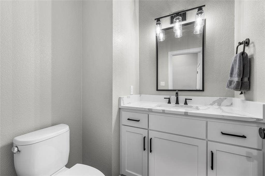 White vanity cabinet with matte black hardware, quartz-composite countertop, undermount sink, three-light linear fixture, and framed wall mirror