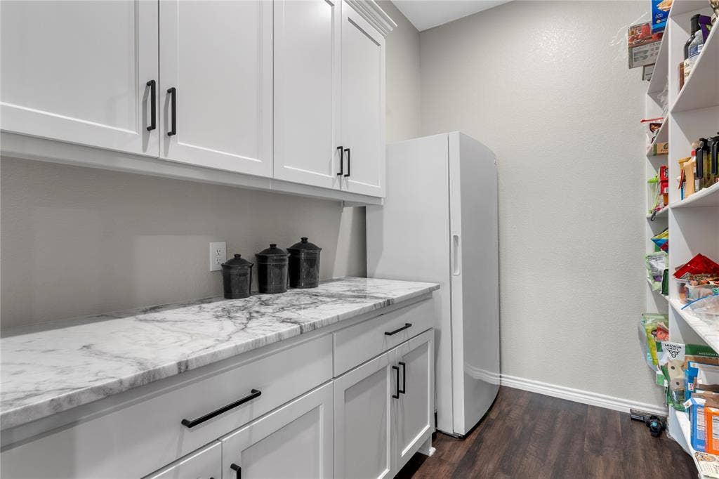Walk-in pantry featuring white shaker-style cabinetry, stone-patterned countertops, dark hardware, wood-finish flooring, and open shelving