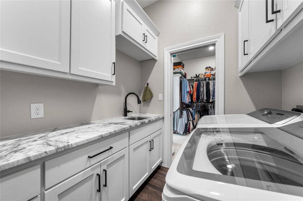 Laundry room featuring white shaker-style cabinetry, stone-finish countertops, an undermount sink with a matte black faucet, and wood-finish flooring