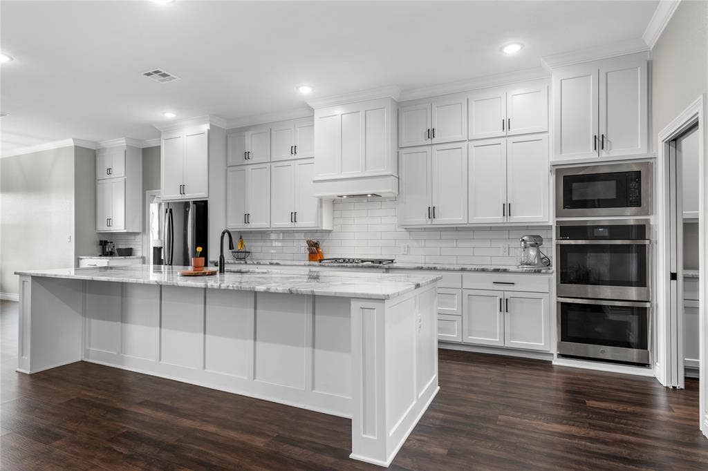 Kitchen featuring white shaker-style cabinetry, a stone-finish waterfall edge island, subway tile backsplash, stainless steel built-in double wall ovens, and wood-finish flooring