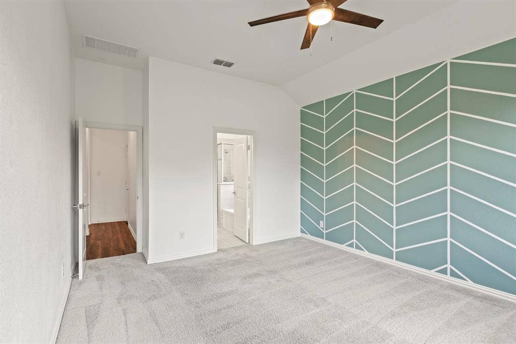 2305 Switchgrass Street, Melissa, TX 75454 Vaulted ceilings featuring an integrated ceiling fan with light fixture, decorative accent wall with geometric pattern, and neutral carpeting