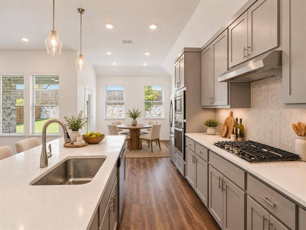 2305 Switchgrass Street, Melissa, TX 75454 Kitchen featuring gray cabinetry, light-toned quartz countertops, a herringbone-pattern backsplash, stainless steel built-in appliances, and wood-finish flooring. Virtual photo