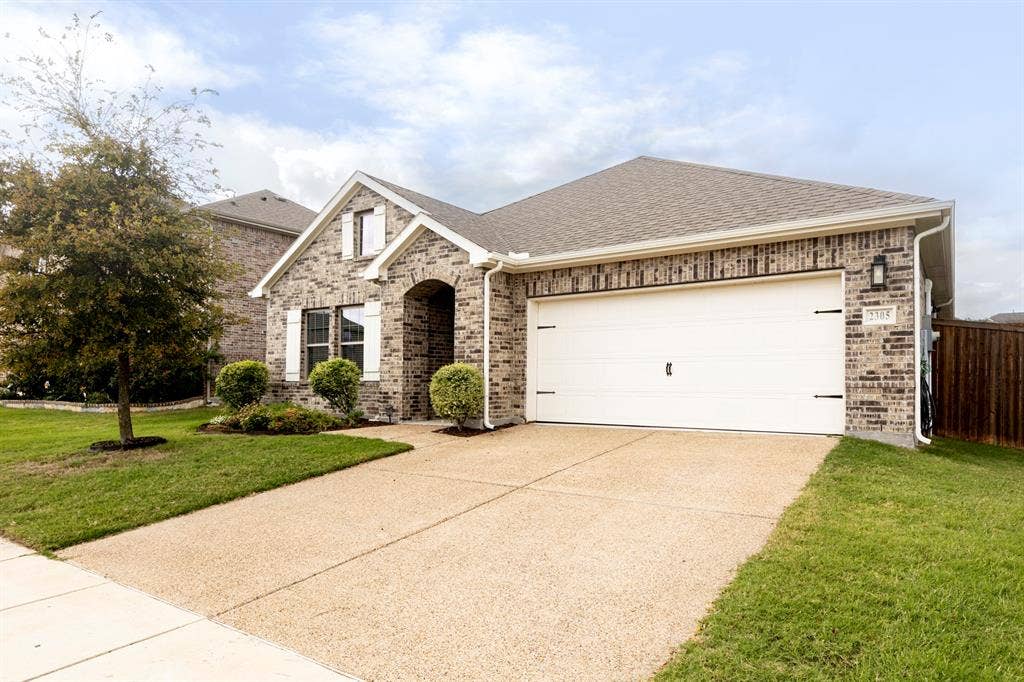 2305 Switchgrass Street, Melissa, TX 75454 Brick exterior residence featuring a front-facing attached garage, arched entryway, white shutter accents, and a concrete driveway