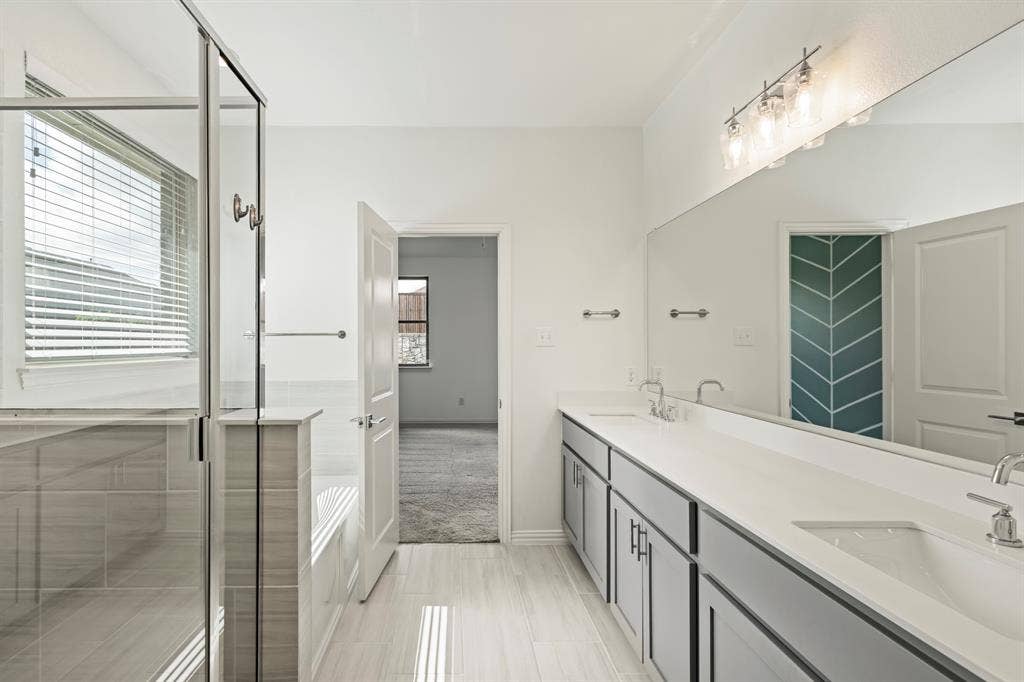 2305 Switchgrass Street, Melissa, TX 75454 Bathroom featuring a dual-sink vanity with solid-surface countertops, a glass-enclosed shower with tile surround, an oversized wall-to-wall mirror, and neutral tile flooring