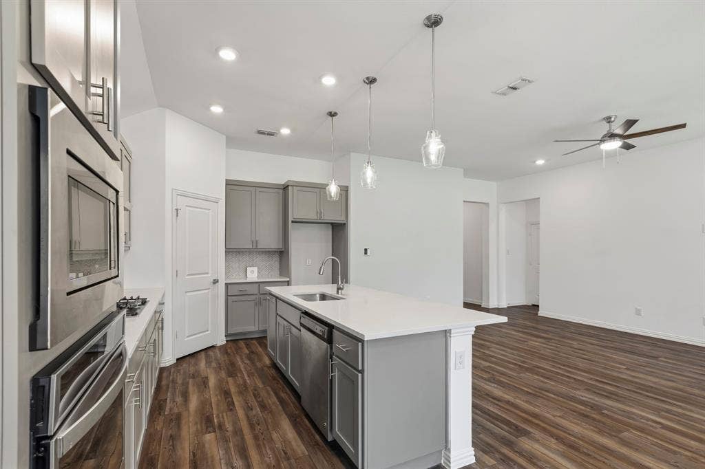 2305 Switchgrass Street, Melissa, TX 75454 Kitchen featuring grey cabinetry, a central island with a solid-surface countertop, stainless steel appliances, pendant lighting, and wood-finish flooring