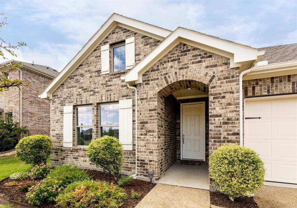 2305 Switchgrass Street, Melissa, TX 75454 Brick exterior featuring a gabled roofline, arched covered entryway, decorative white shutters, and a concrete walkway