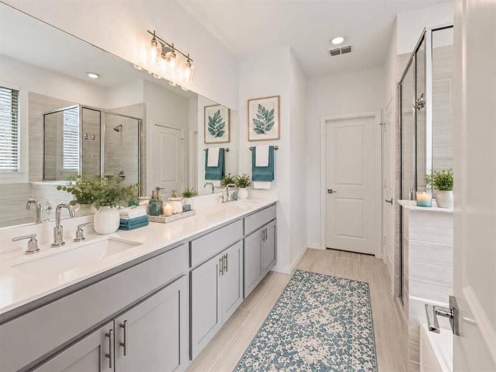 2305 Switchgrass Street, Melissa, TX 75454 Bathroom featuring a dual-sink vanity with light gray cabinetry and white countertops, a large wall-to-wall vanity mirror, polished chrome plumbing fixtures, and a glass-enclosed shower with horizontal tile surround. Virtual photo