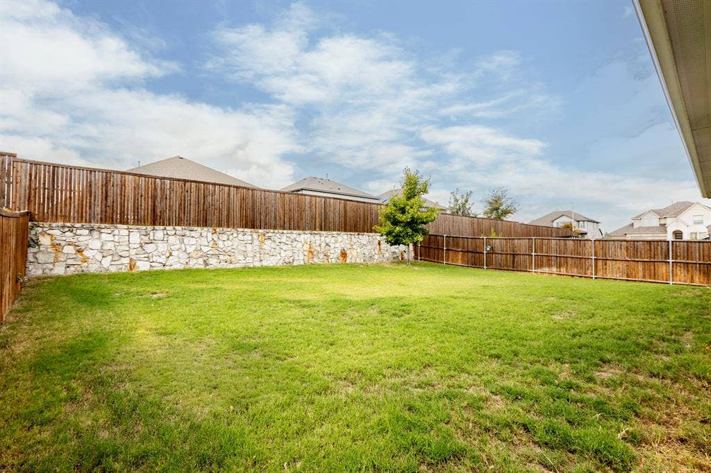 2305 Switchgrass Street, Melissa, TX 75454 Backyard featuring a leveled lawn, natural stone retaining wall, and full-perimeter wood fencing
