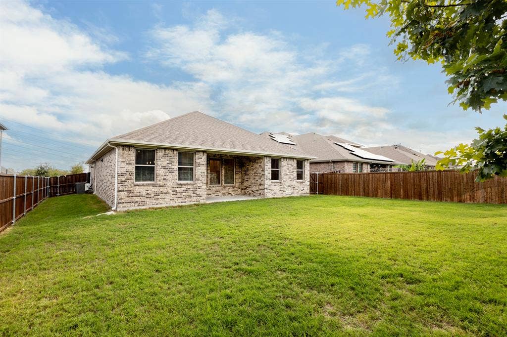 2305 Switchgrass Street, Melissa, TX 75454 Brick exterior featuring a covered patio, gabled roofline, and wood privacy fencing enclosing a lawn