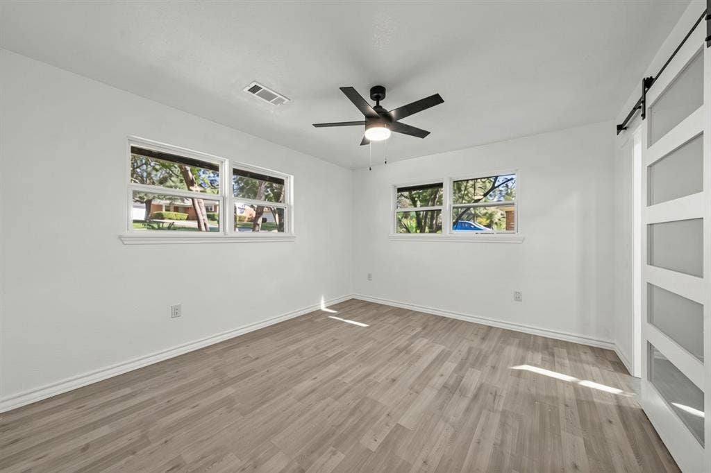 Interior space featuring wood-finish flooring, a ceiling fan with integrated lighting, dual-pane windows, and a white sliding barn door with frosted glass panels