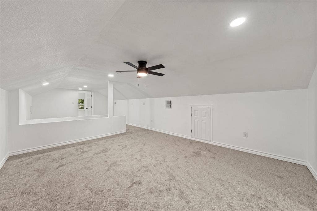 Finished attic space featuring vaulted ceilings, neutral carpeting, a central ceiling fan, and built-in eave storage access
