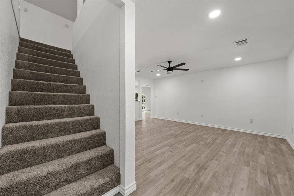 Staircase with plush carpeted steps, wood-finish flooring, recessed lighting, and a matte black ceiling fan