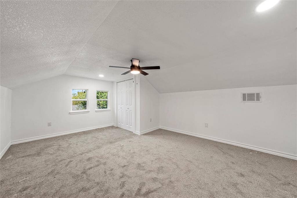 Interior room featuring vaulted ceilings, neutral wall-to-wall carpeting, recessed lighting, a ceiling fan with integrated light fixture, and two double-door closet configurations