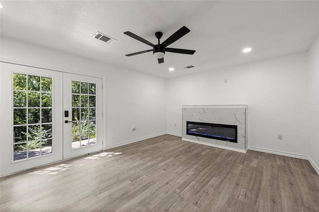 Wood-finish flooring, recessed lighting, matte black ceiling fan, dual-pane French doors, and built-in electric fireplace with stone-pattern surround