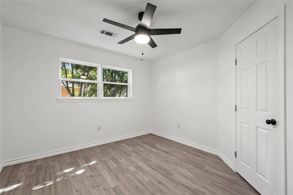 Interior space featuring wood-finish flooring, a matte black multi-blade ceiling fan with integrated lighting, and a six-panel door with matte black hardware