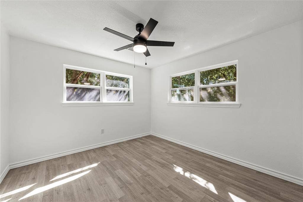 Neutral interior featuring light-toned wood-finish flooring, white walls, and a modern ceiling fan with integrated lighting, complemented by dual windows