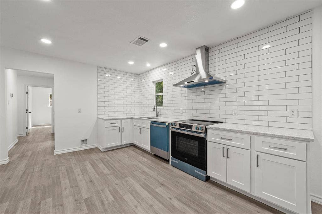 Kitchen featuring white shaker-style cabinetry, stone-finish countertops, full-height white subway tile backsplash, stainless steel range hood, and wood-finish flooring
