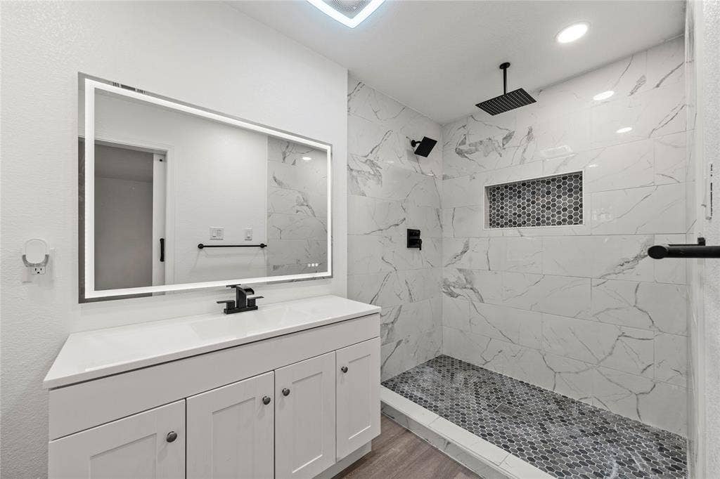 White shaker-style vanity with a solid surface countertop, LED-backlit mirror, and matte black hardware
