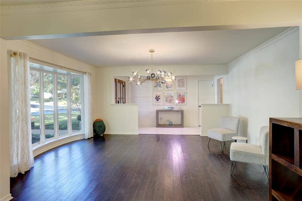 Open-concept space featuring dark wood-finish flooring, a large multi-pane bay window, crown molding, and a tiered modern sputnik chandelier