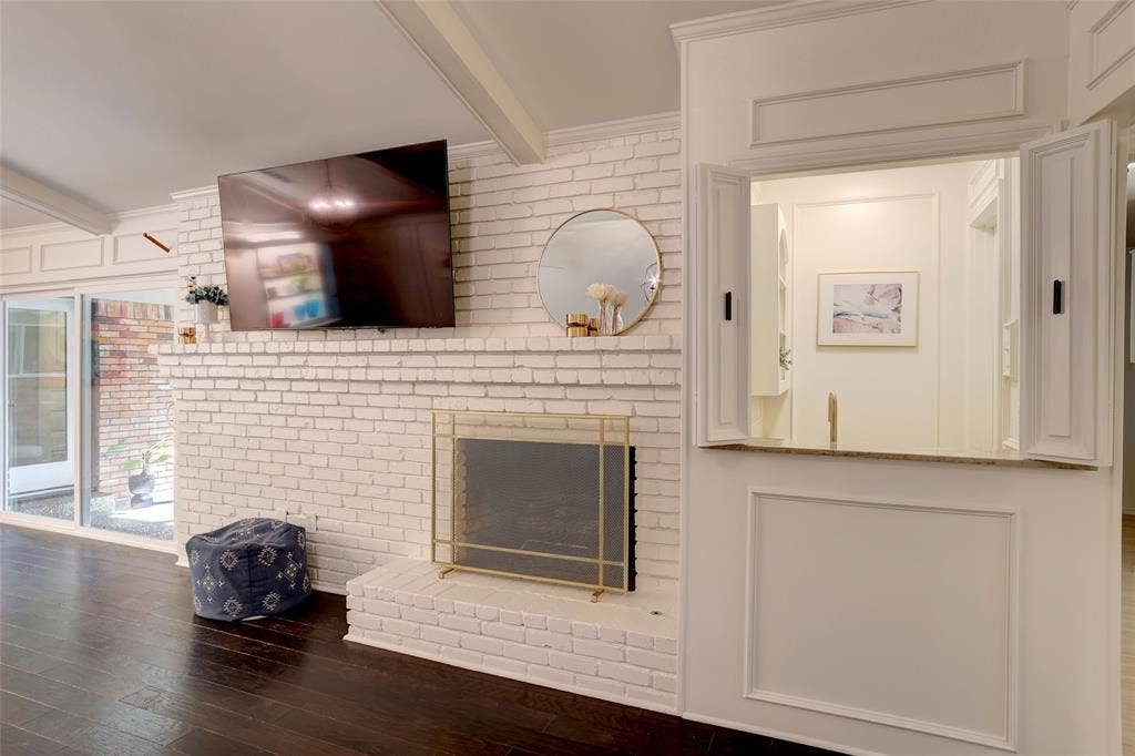 White-painted brick fireplace with a raised hearth and gold-tone metal screen, integrated wall cabinetry with paneled doors, and dark wood-finish flooring