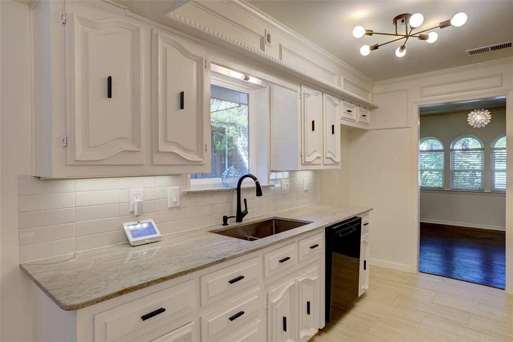 Custom white cabinetry with black hardware, stone countertops, subway tile backsplash, stainless steel undermount sink, and contemporary multi-arm ceiling fixture