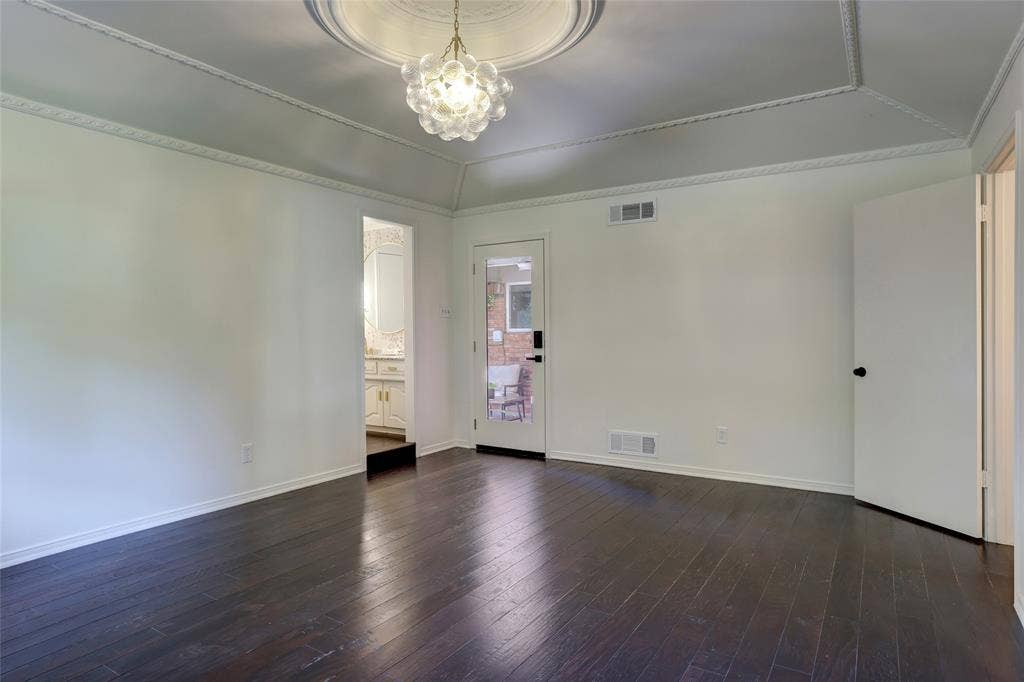 Tray ceiling featuring intricate crown molding and a decorative central medallion with a multi-globe glass pendant light, complemented by dark wood-finish flooring