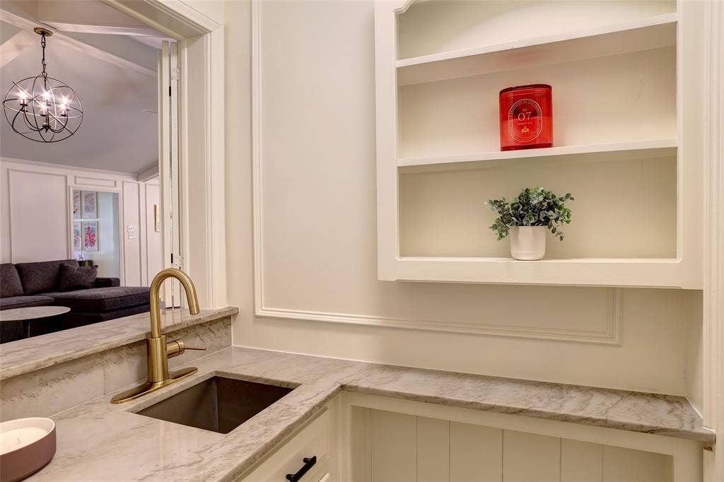 Built-in recessed shelving, stone countertop, undermount sink with brass-finish faucet, and wainscoting detail