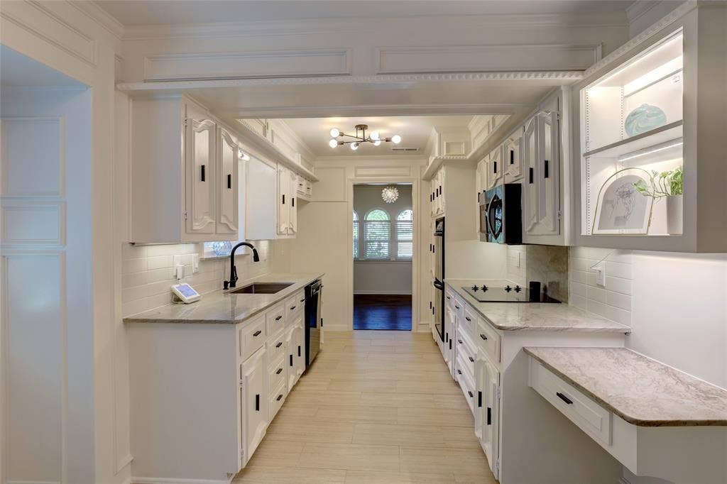 Kitchen featuring custom white cabinetry with integrated lighting, stone-finish countertops, subway tile backsplash, matte black hardware, and light-tone wood-finish flooring