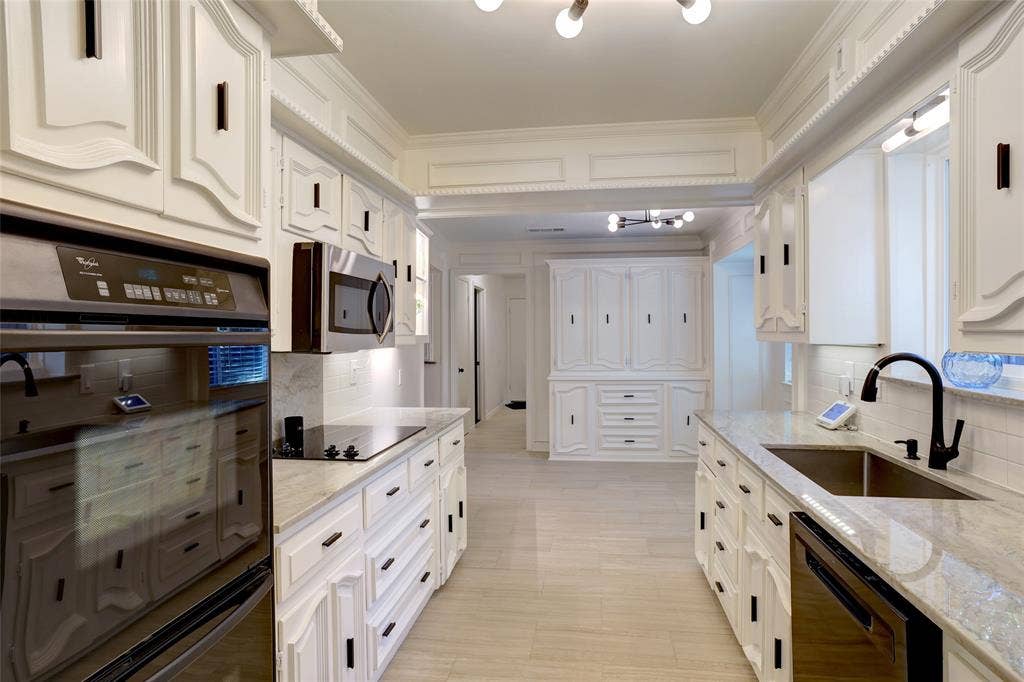 Kitchen featuring white custom cabinetry with matte black hardware, stone countertops, stainless steel wall-mounted oven and microwave, tiled backsplash, and wood-finish flooring