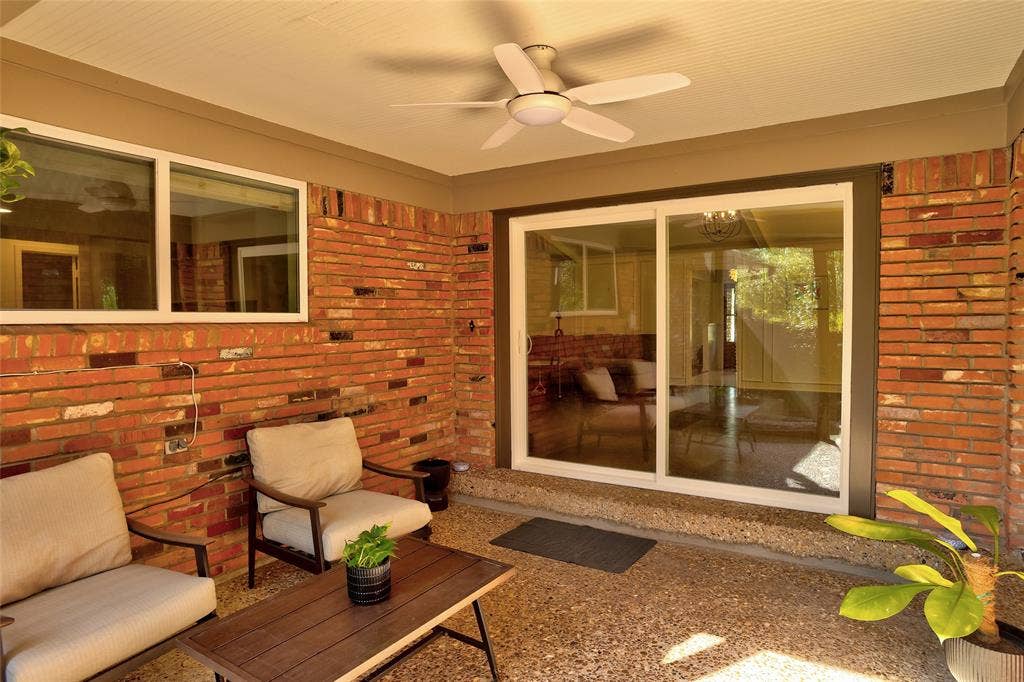 Covered patio featuring red brick walls, exposed-aggregate concrete flooring, a ceiling fan with integrated lighting, and sliding glass doors
