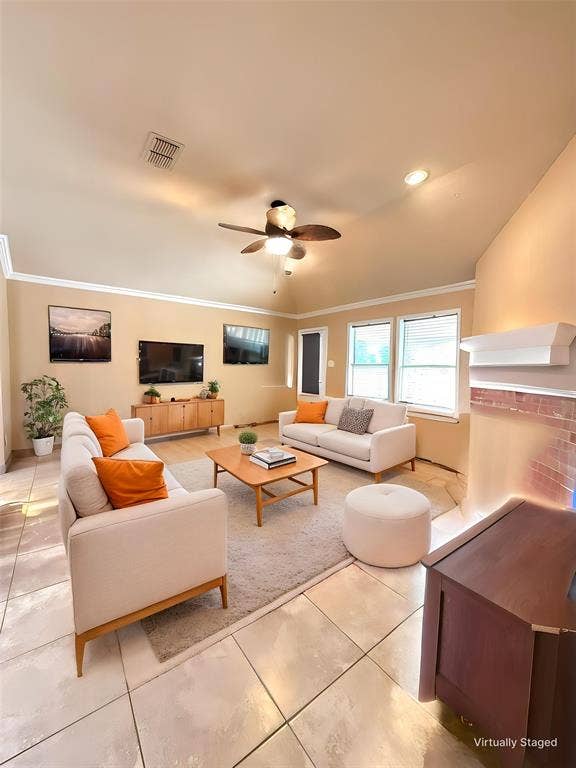 Living area featuring a vaulted ceiling, tile flooring, crown molding, and a brick-accented fireplace with a mantel