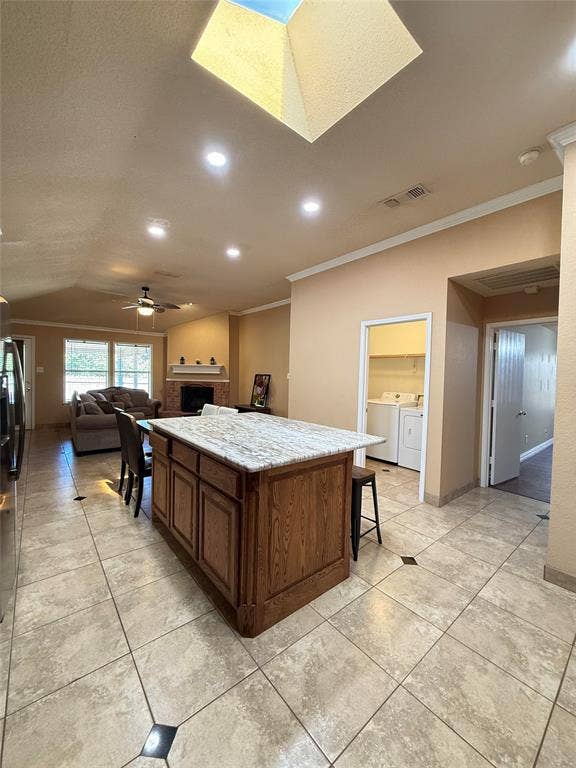 Kitchen featuring a central island with a stone-finish countertop and wood cabinetry, overhead skylight, recessed lighting, and tile flooring with decorative inlay accents
